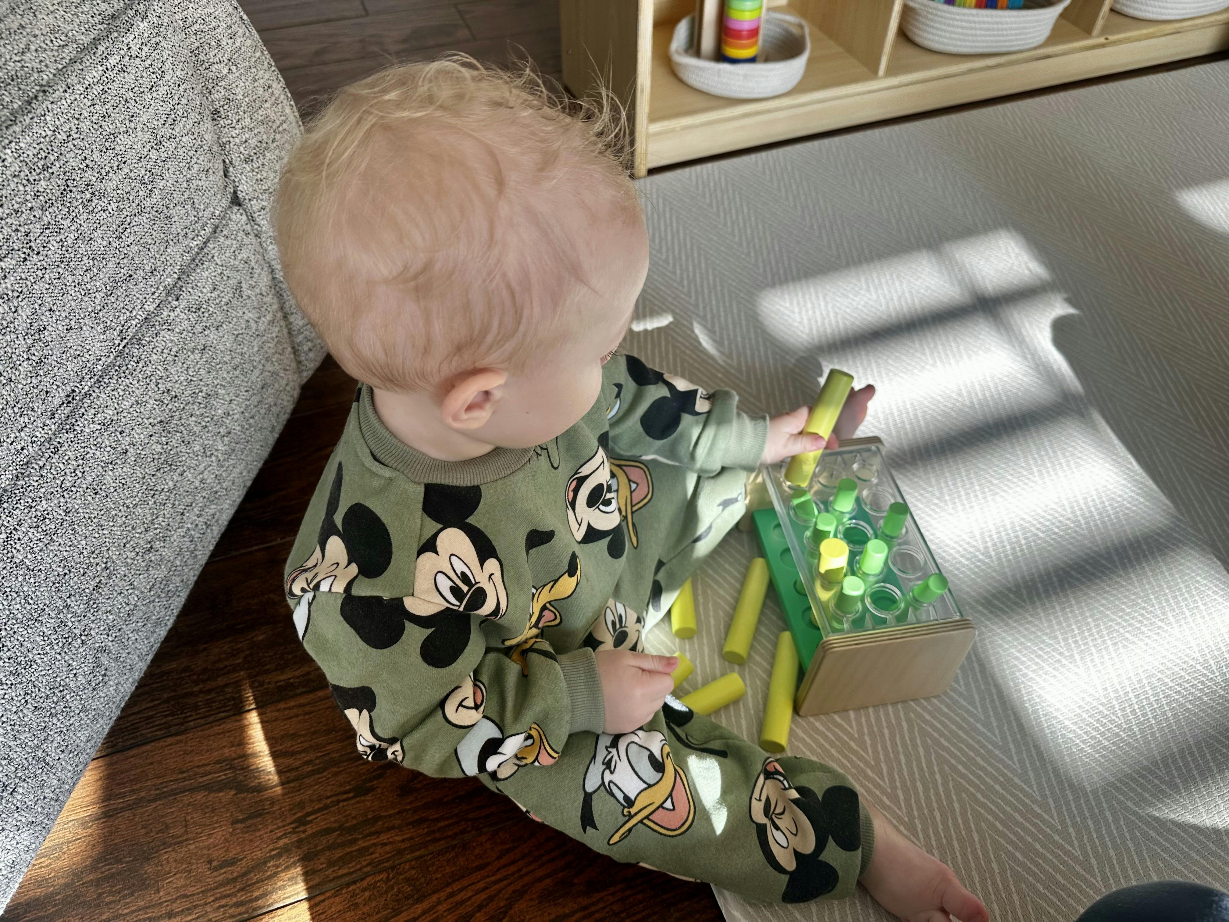 Child sitting on floor playing with green and yellow peg toy