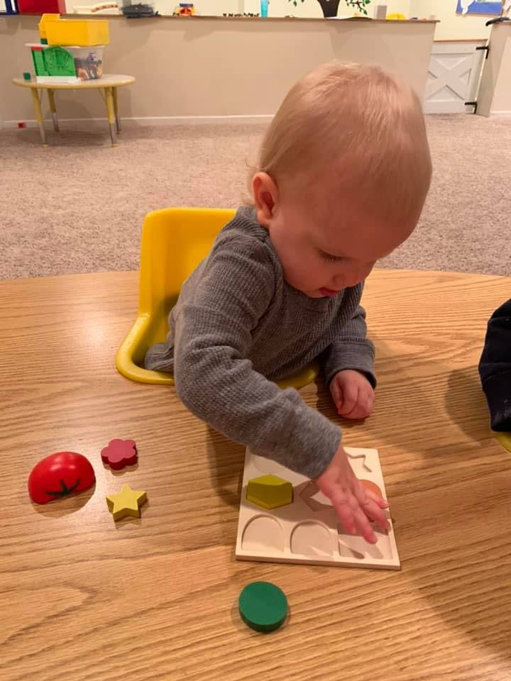 Child playing with a wooden shape sorter puzzle on a table