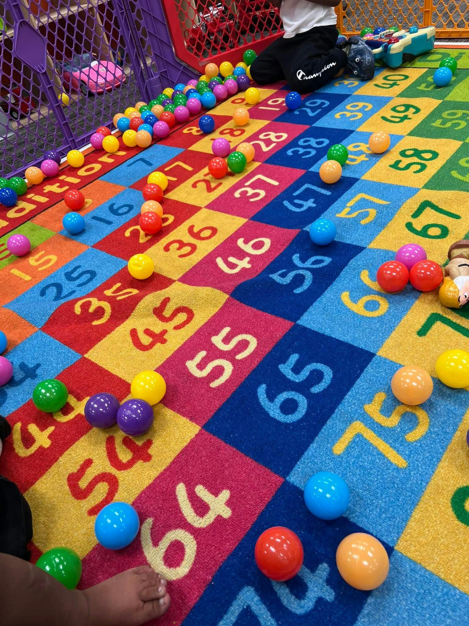 Child sitting on a colorful numbered rug with many small balls