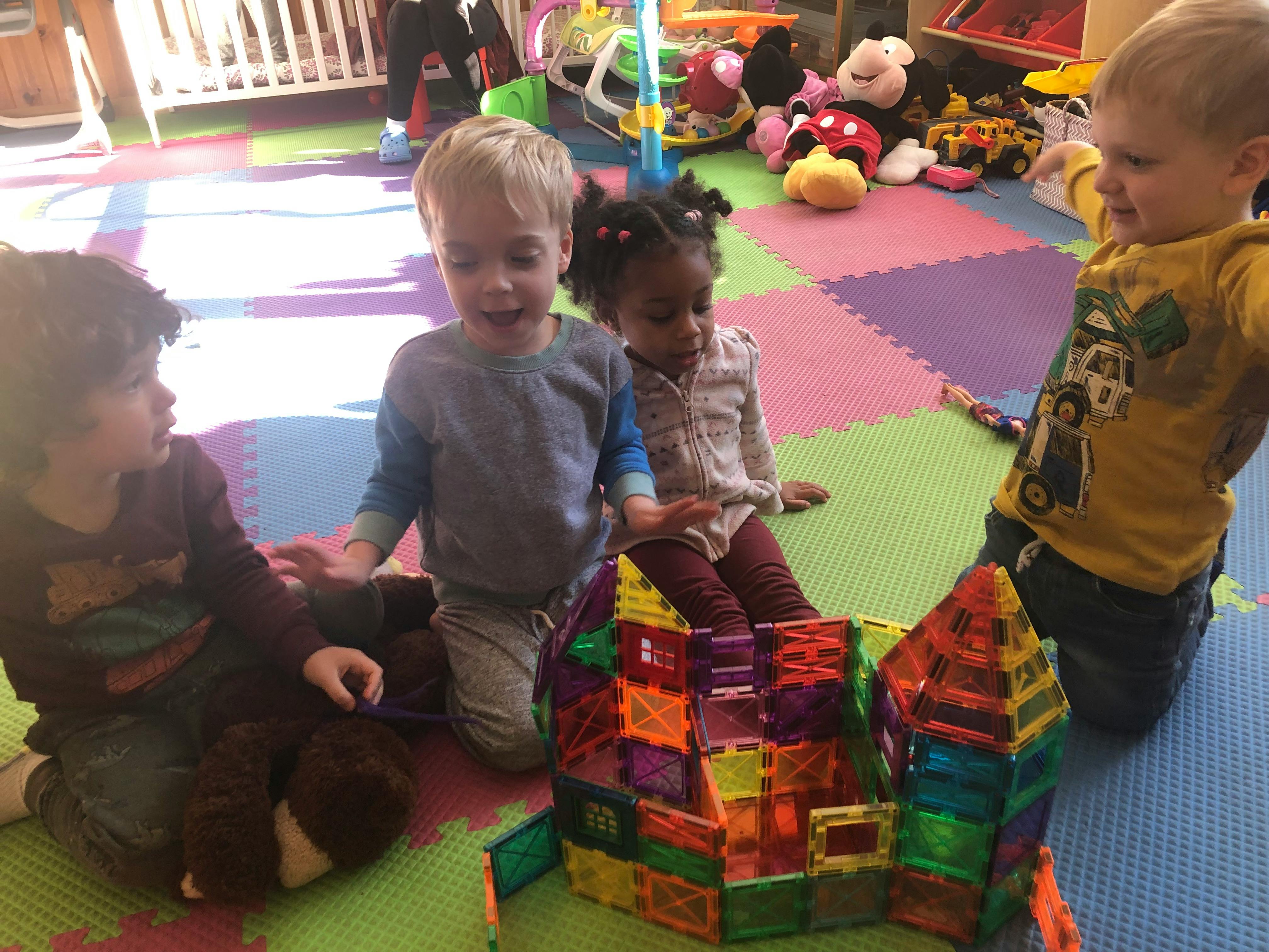 Four children playing with colorful magnetic blocks on a mat