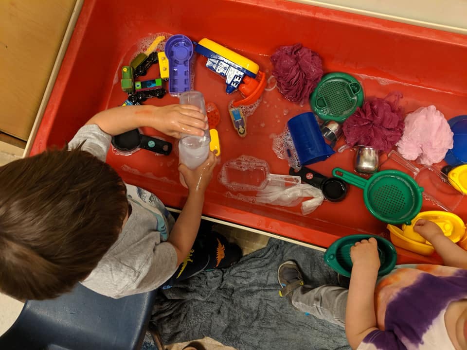 Child playing with water and toys in a red bin