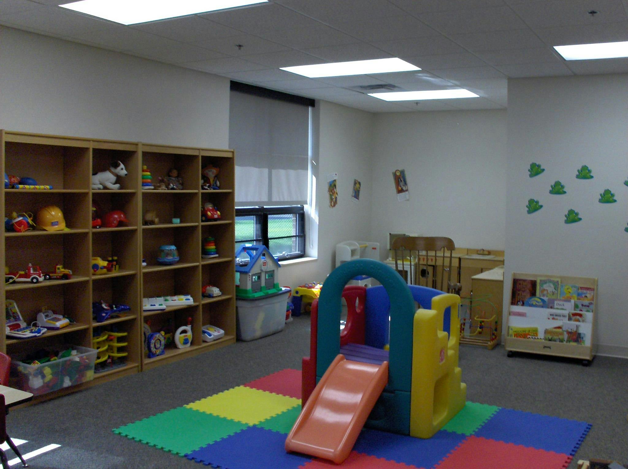 Indoor play area with shelves of toys, a colorful slide, and play mats