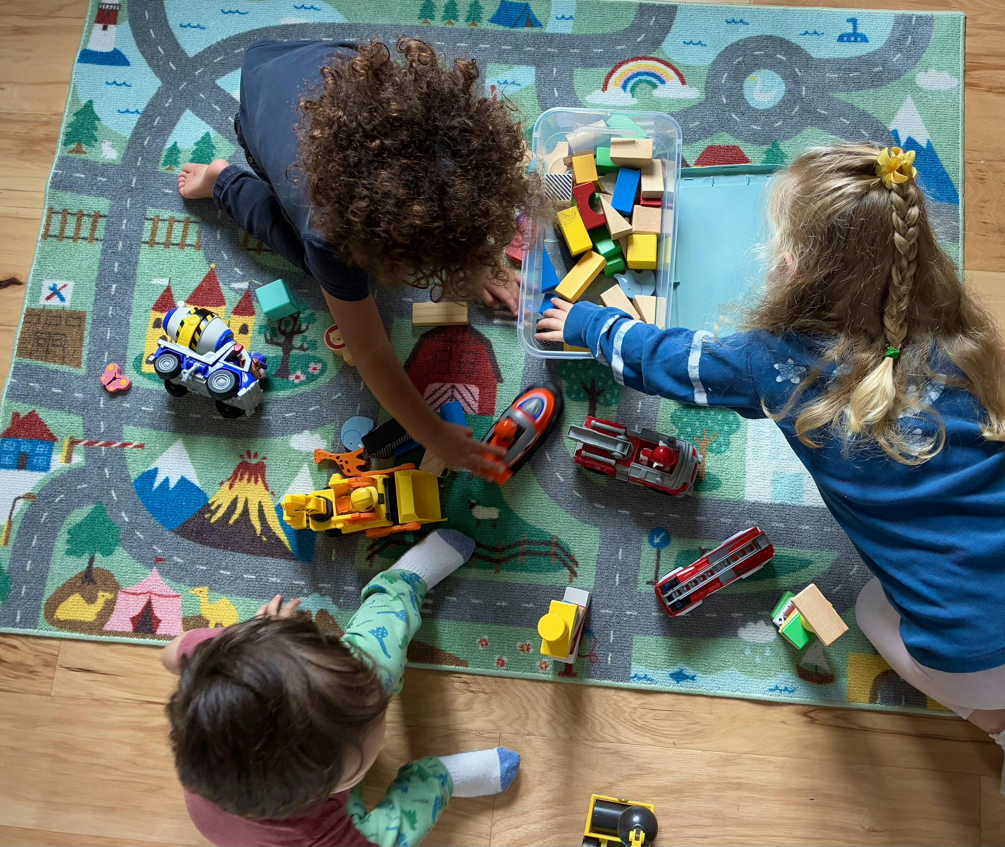 Three children playing with toy vehicles and building blocks on a play rug