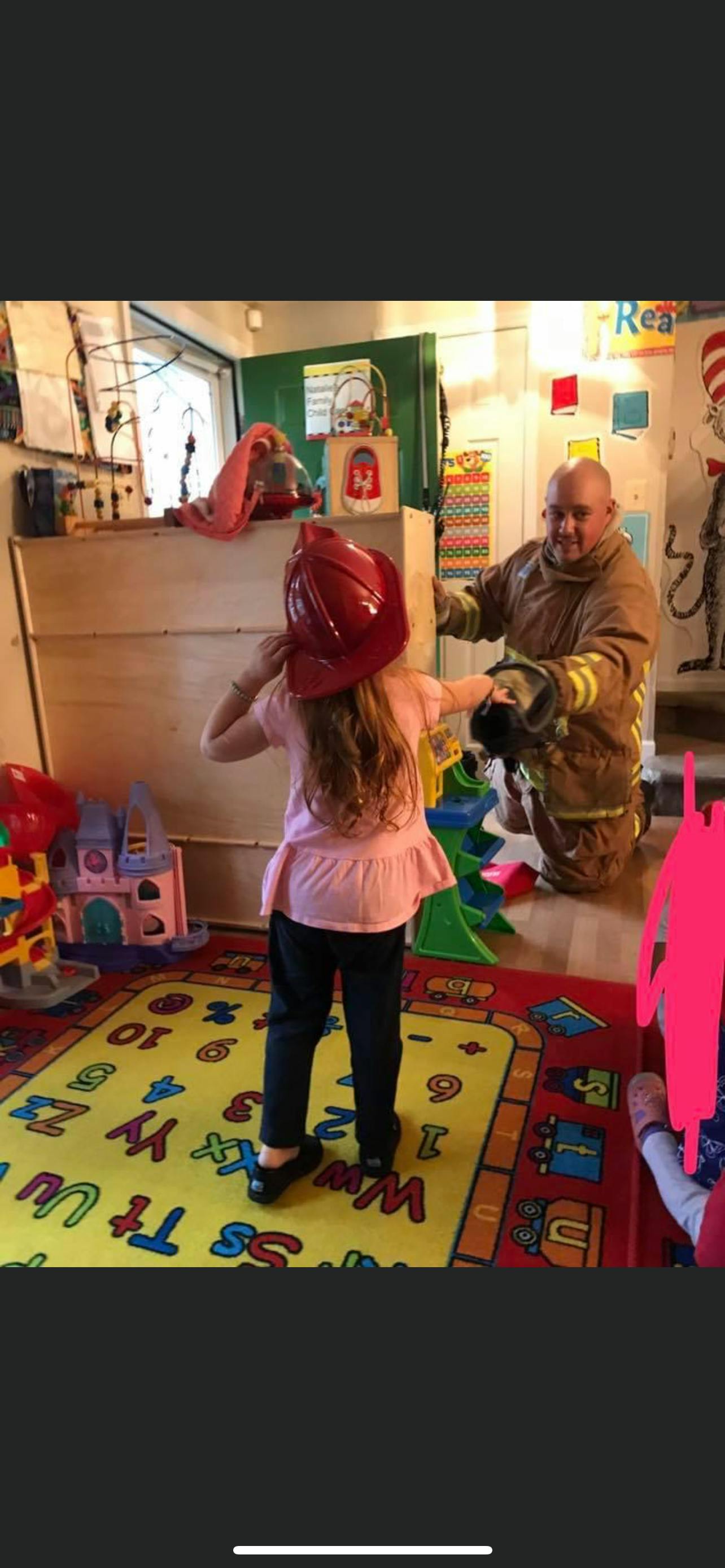 Child wearing a red firefighter helmet with a firefighter in uniform