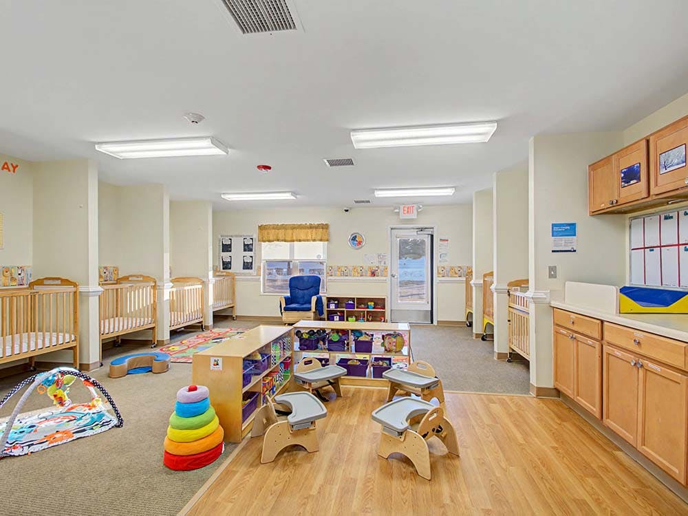 Classroom with multiple cribs, low tables, and play mats