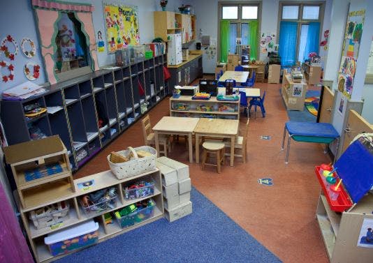 Classroom with small tables and chairs, storage shelves, and colorful decorations