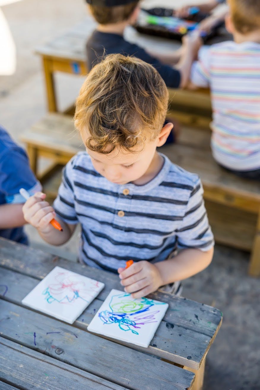 Child drawing on tiles with markers at a table