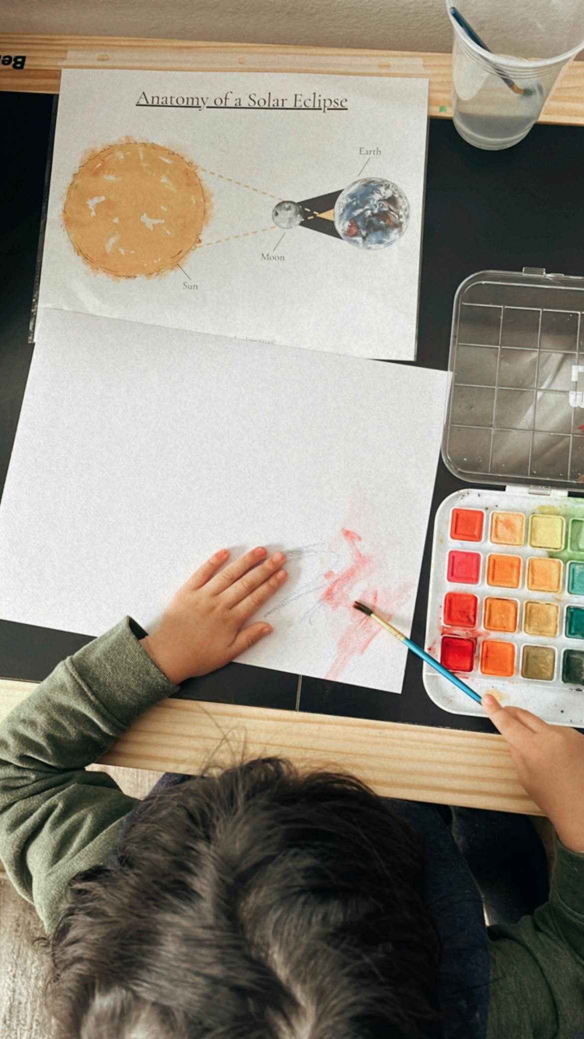 Child painting with watercolors next to a diagram of a solar eclipse