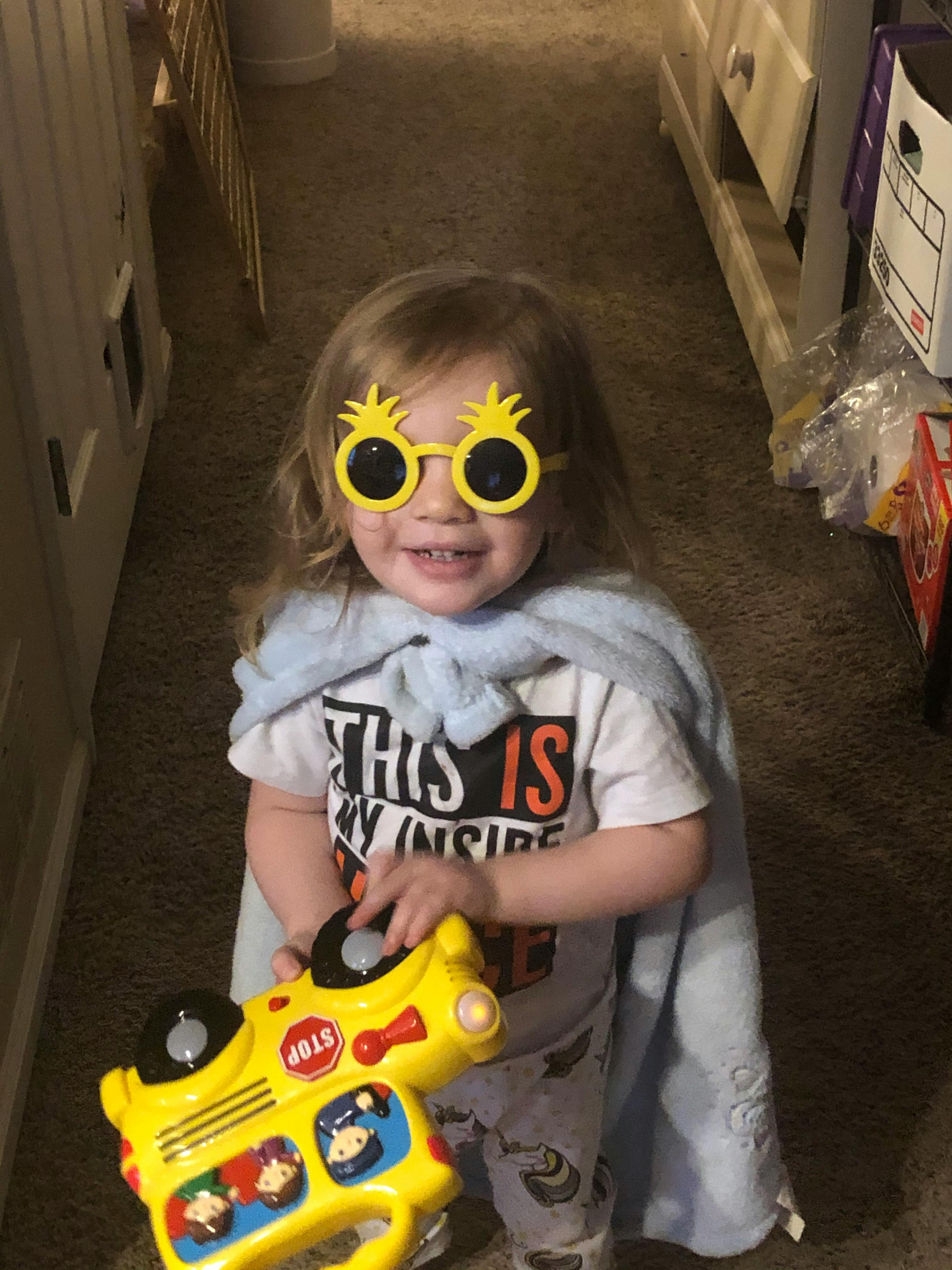 Child wearing novelty sunglasses and a blanket cape holding a toy school bus