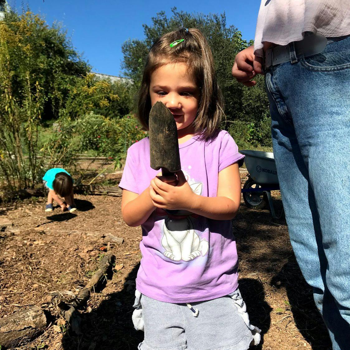Child holding a small shovel in a garden