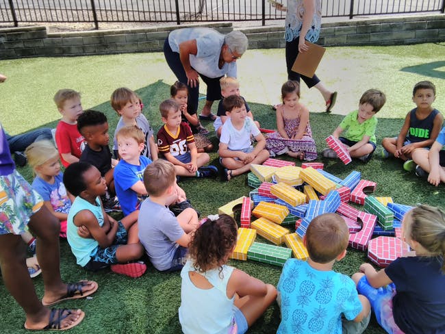 Adults and children sitting on grass with colorful blocks