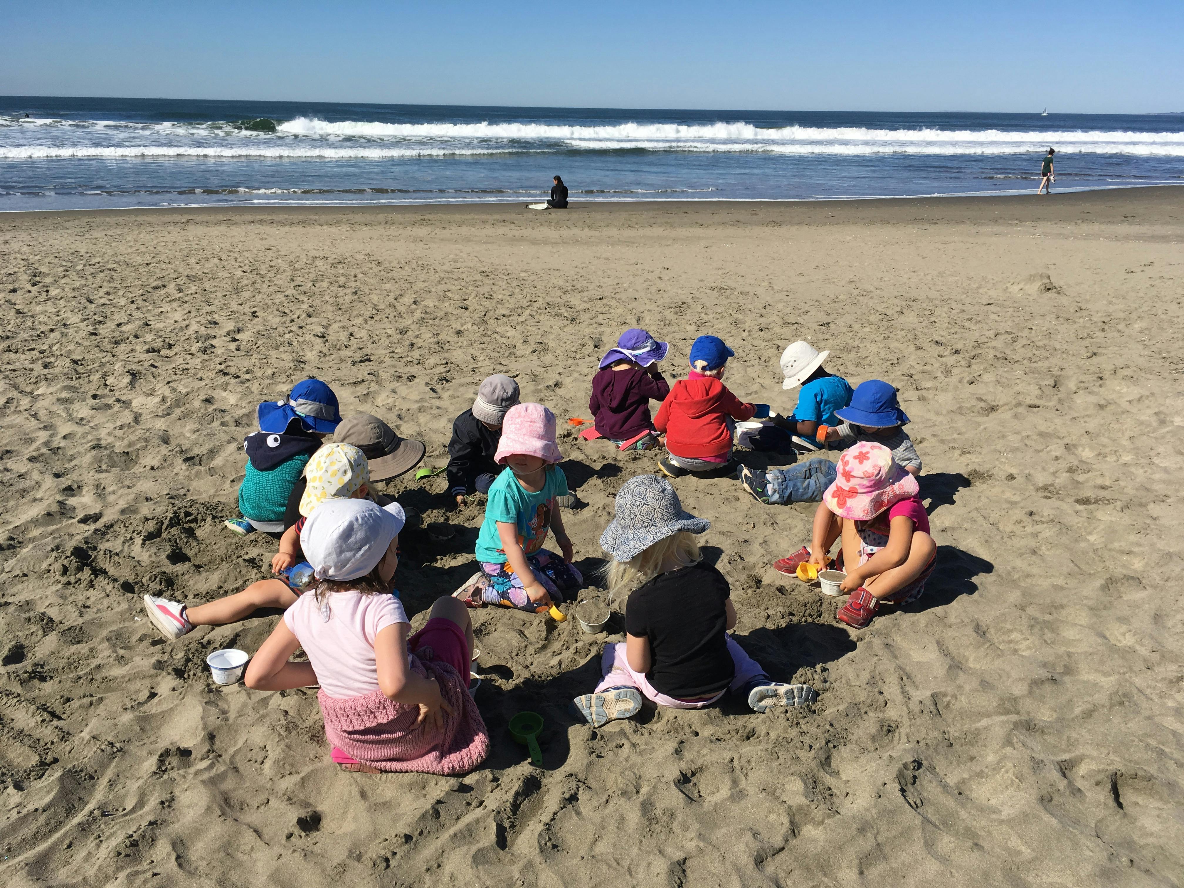 Children sitting in a circle on a sandy beach near the ocean