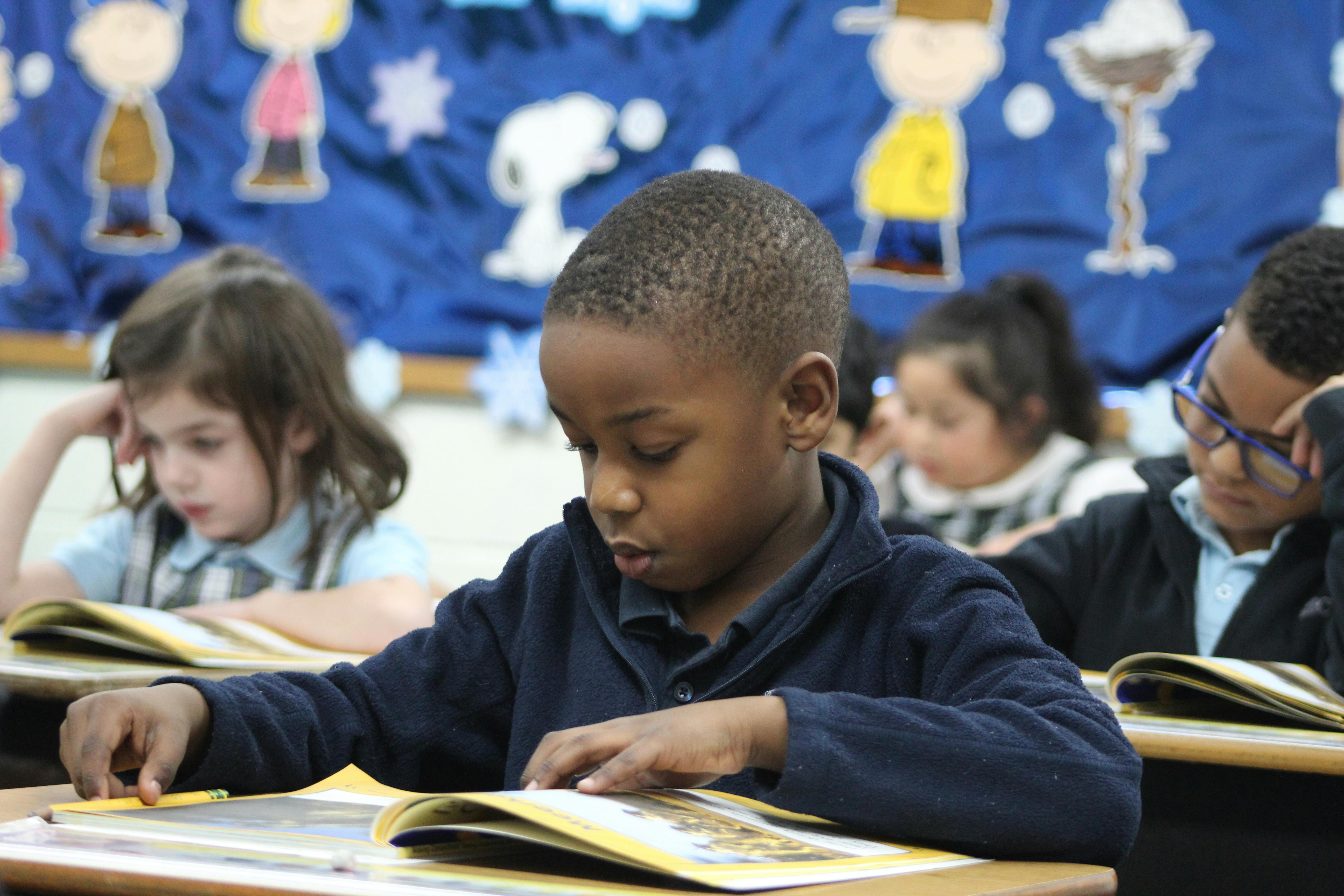 Child reading a book at a desk in a classroom