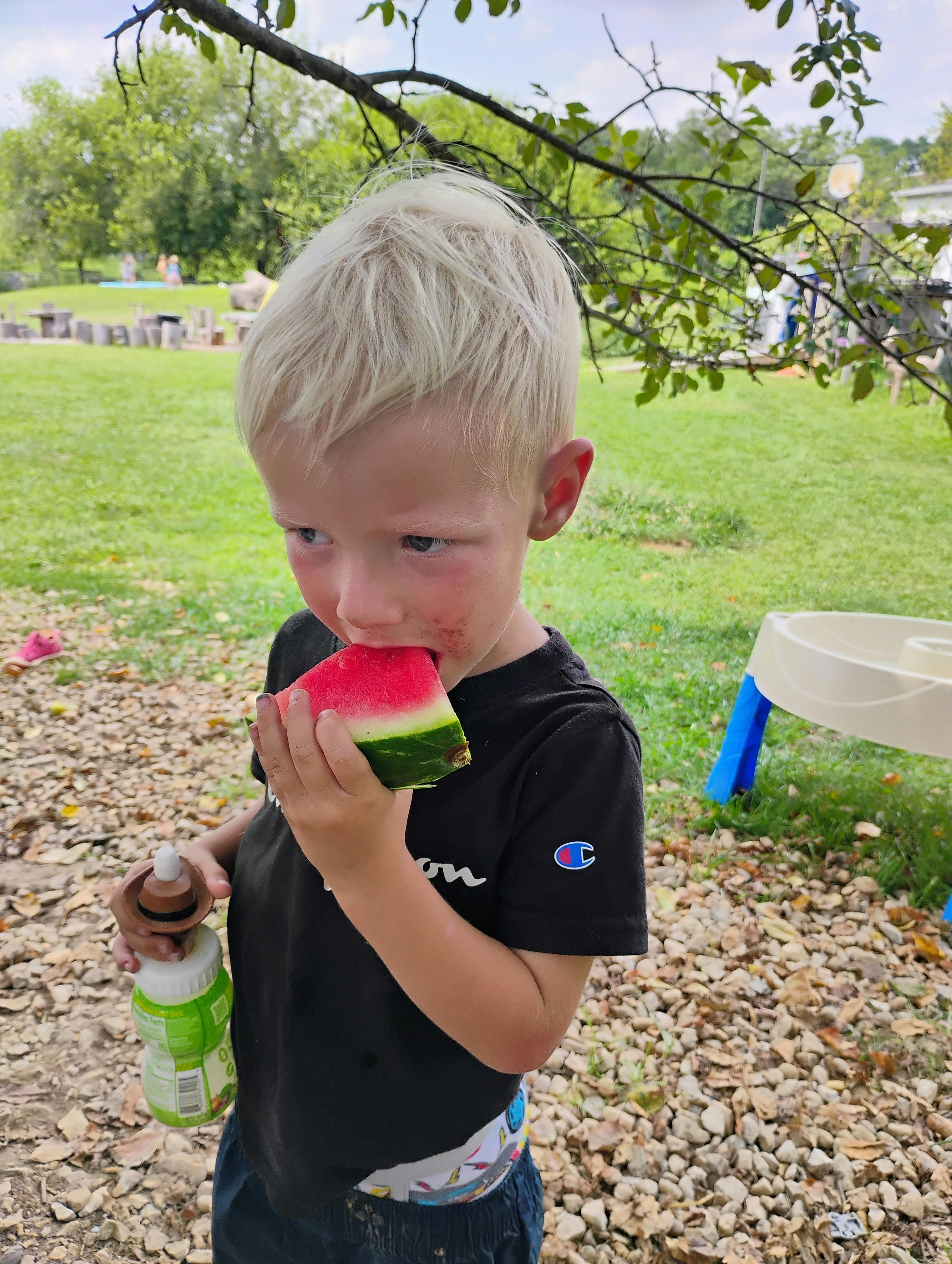 Child eating a slice of watermelon outdoors