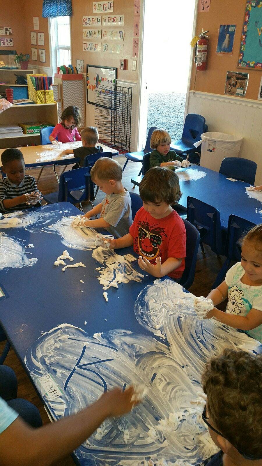 Children playing with shaving cream on a blue table in a classroom