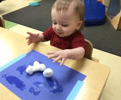 Child at a table with cotton balls and blue paper