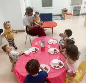 Adult and children gathered around tables in a classroom