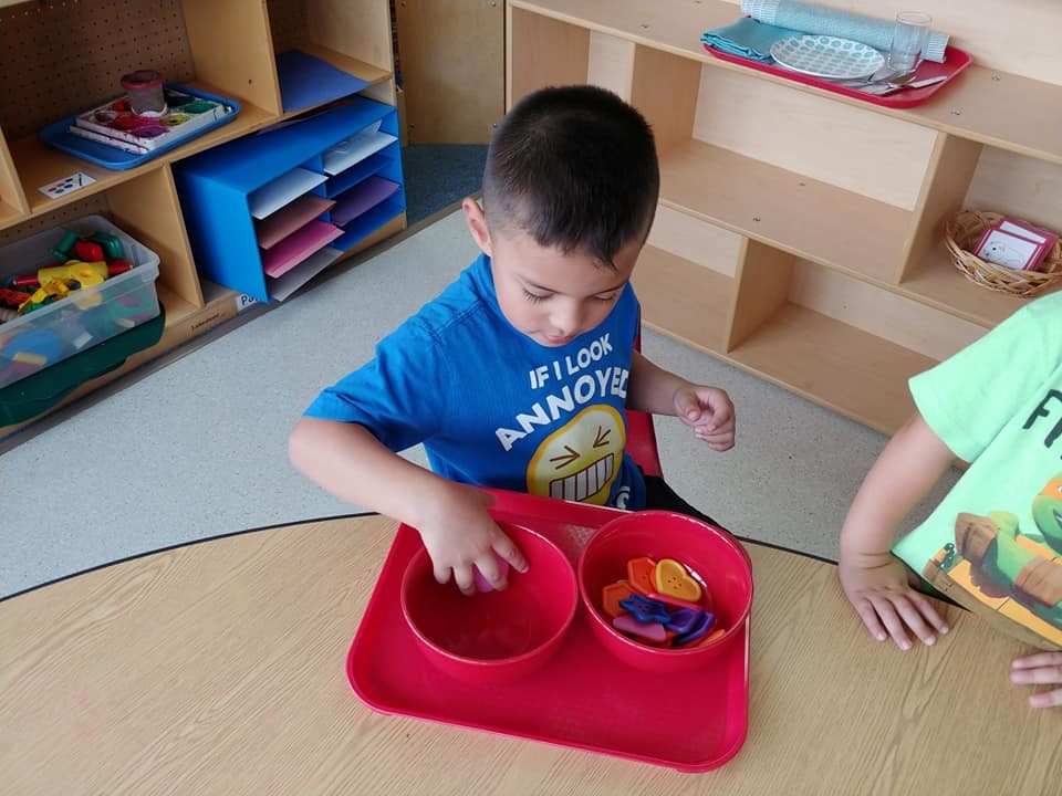 Child playing with bowls and small objects in a classroom