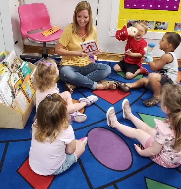 Person reading a book to a group of children sitting on the floor