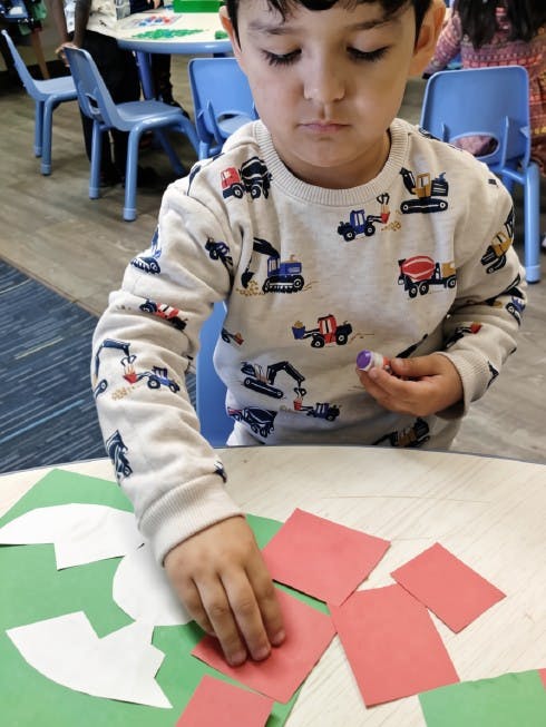 Child gluing red paper squares onto a green craft project