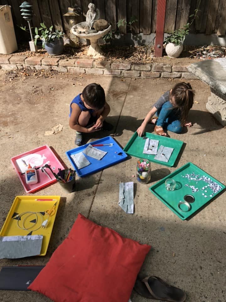 Two children on the ground with craft supplies in trays