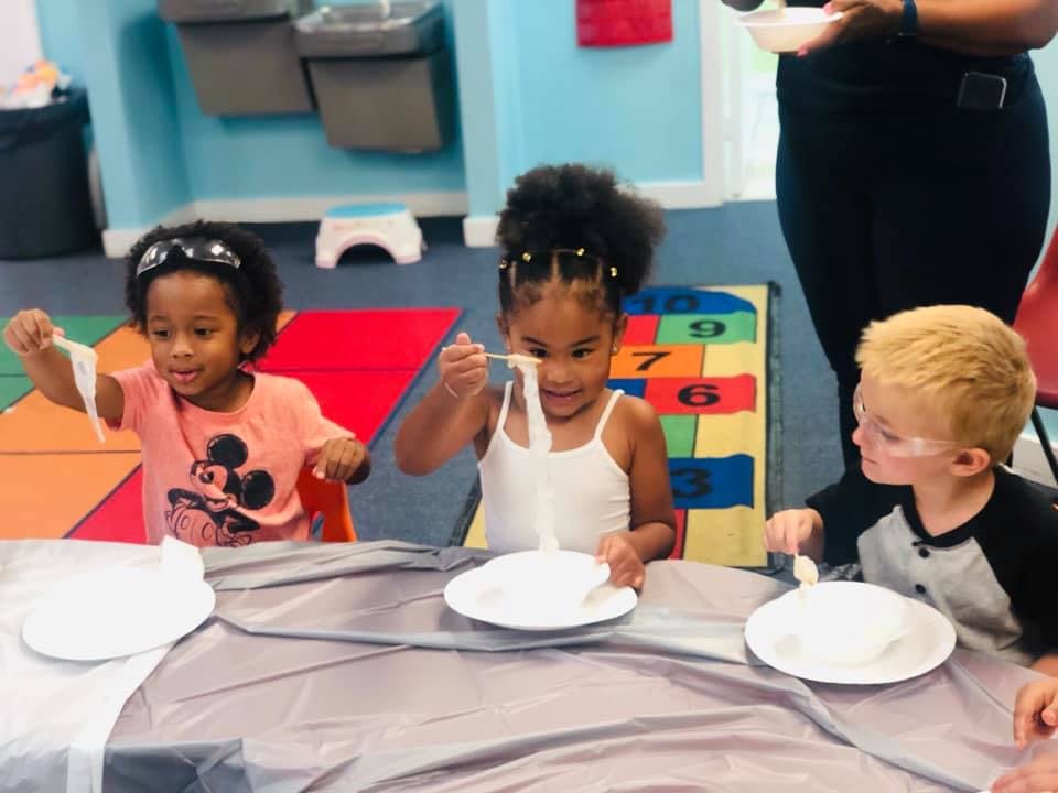 Three children playing with white stringy material at a table