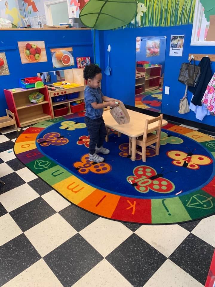 Child standing at a small table in a classroom