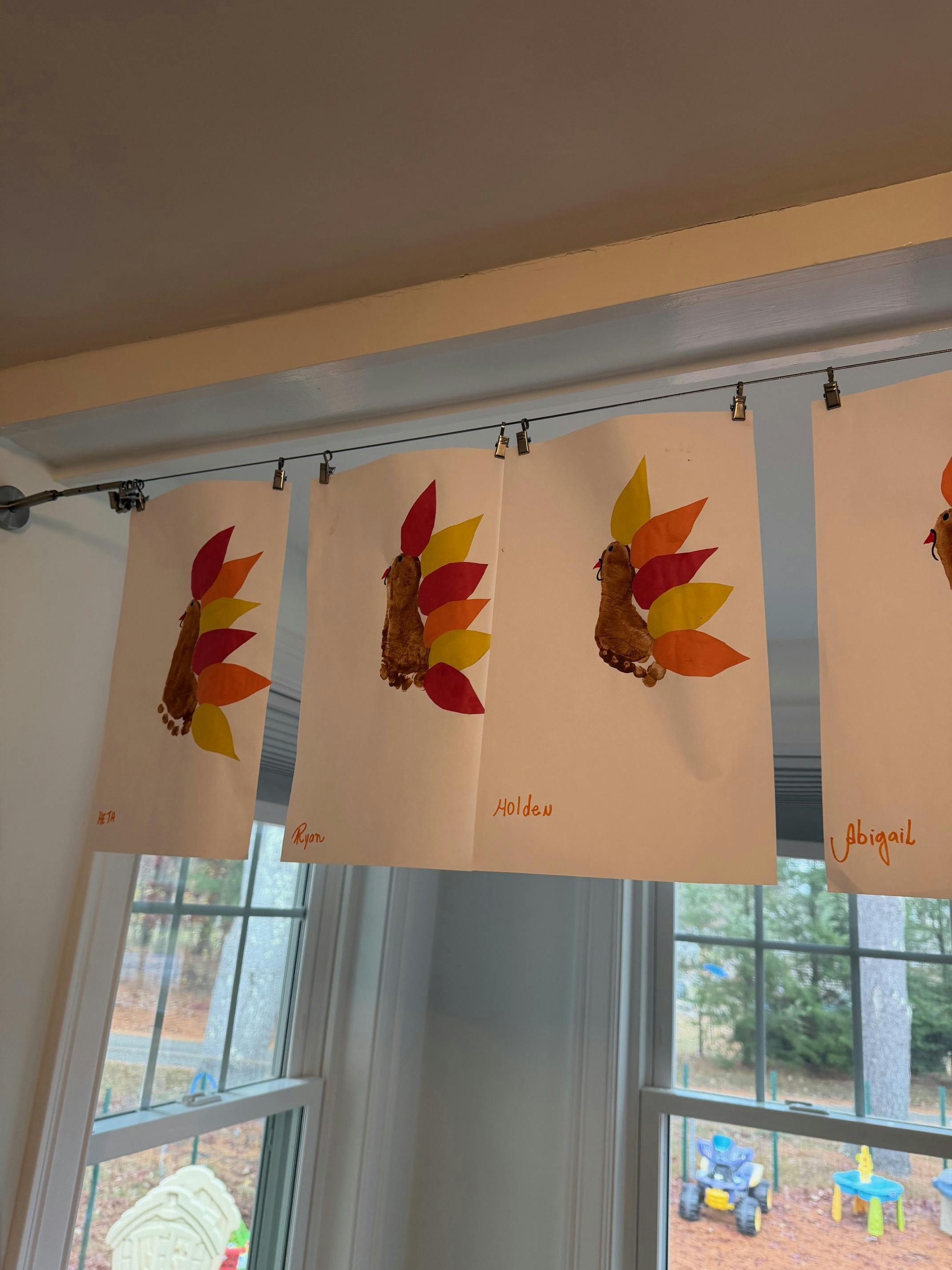 Multiple turkey crafts made from footprints and paper leaves hanging on a wire