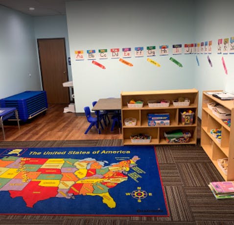 Classroom with a map rug, small tables and chairs, and shelves with supplies