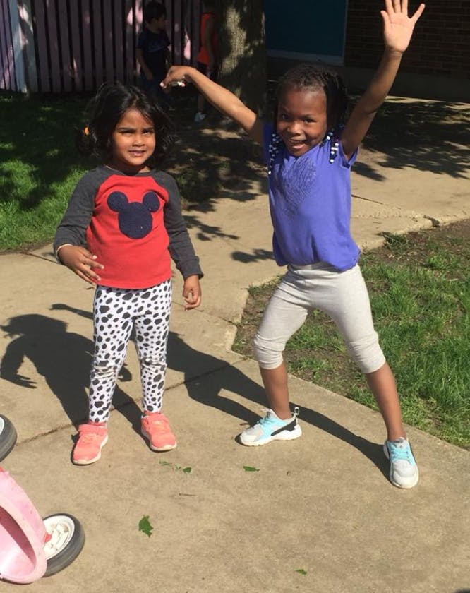 Two children standing outdoors, one with arms raised