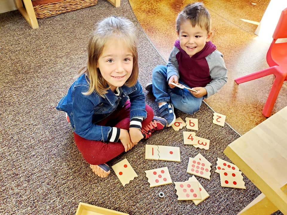 Two children sitting on the floor playing with number and letter tiles