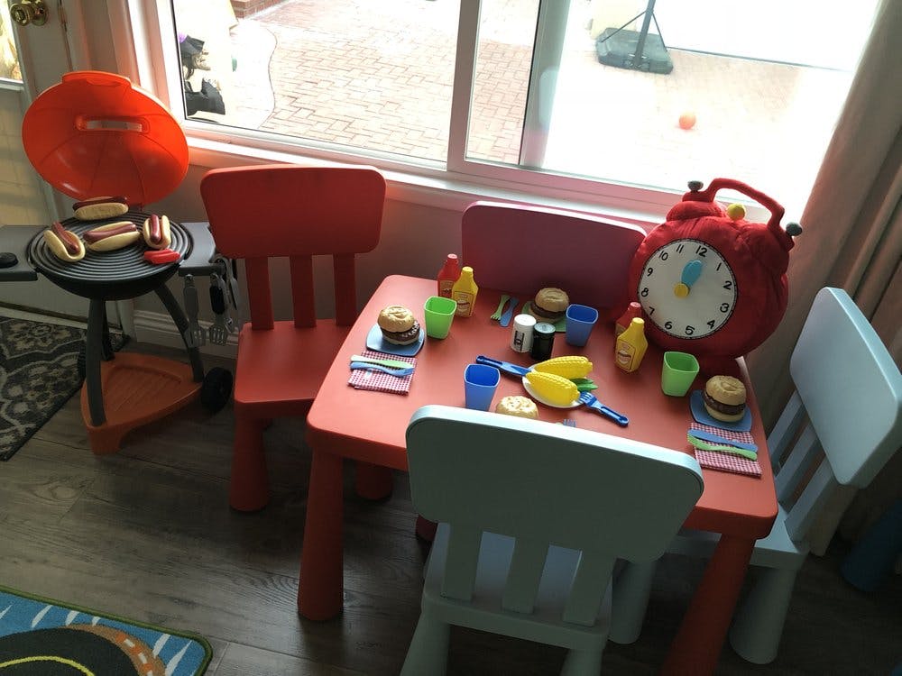 Toy table and chairs with play food and a toy grill with hot dogs