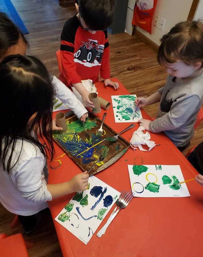 Children painting with various tools in a classroom