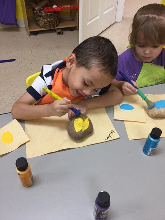 Two children painting rocks at a table