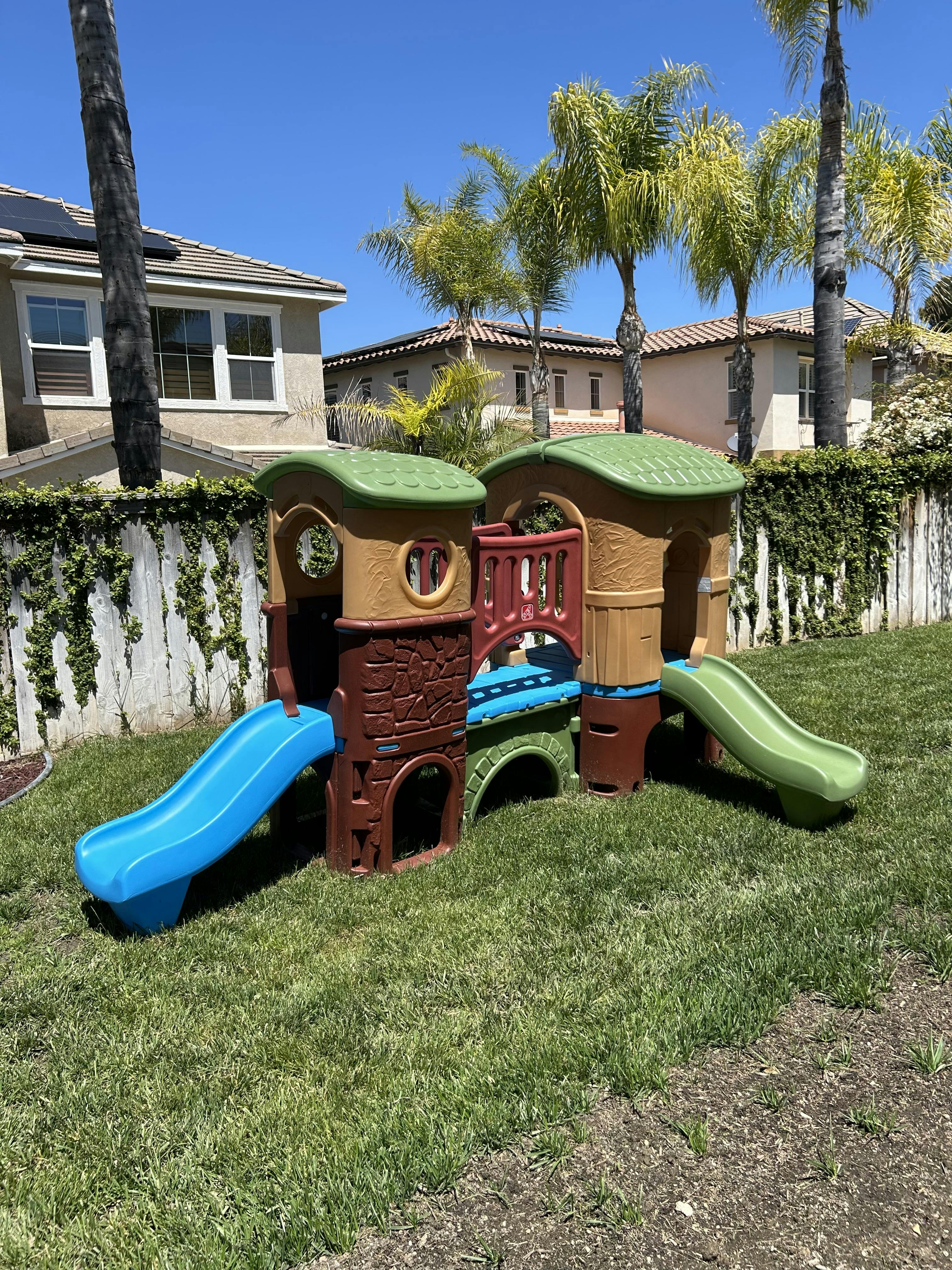 Plastic outdoor playset with two slides in a grassy backyard