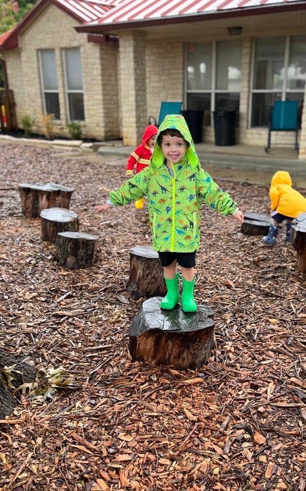 Child in green raincoat and boots standing on a tree stump