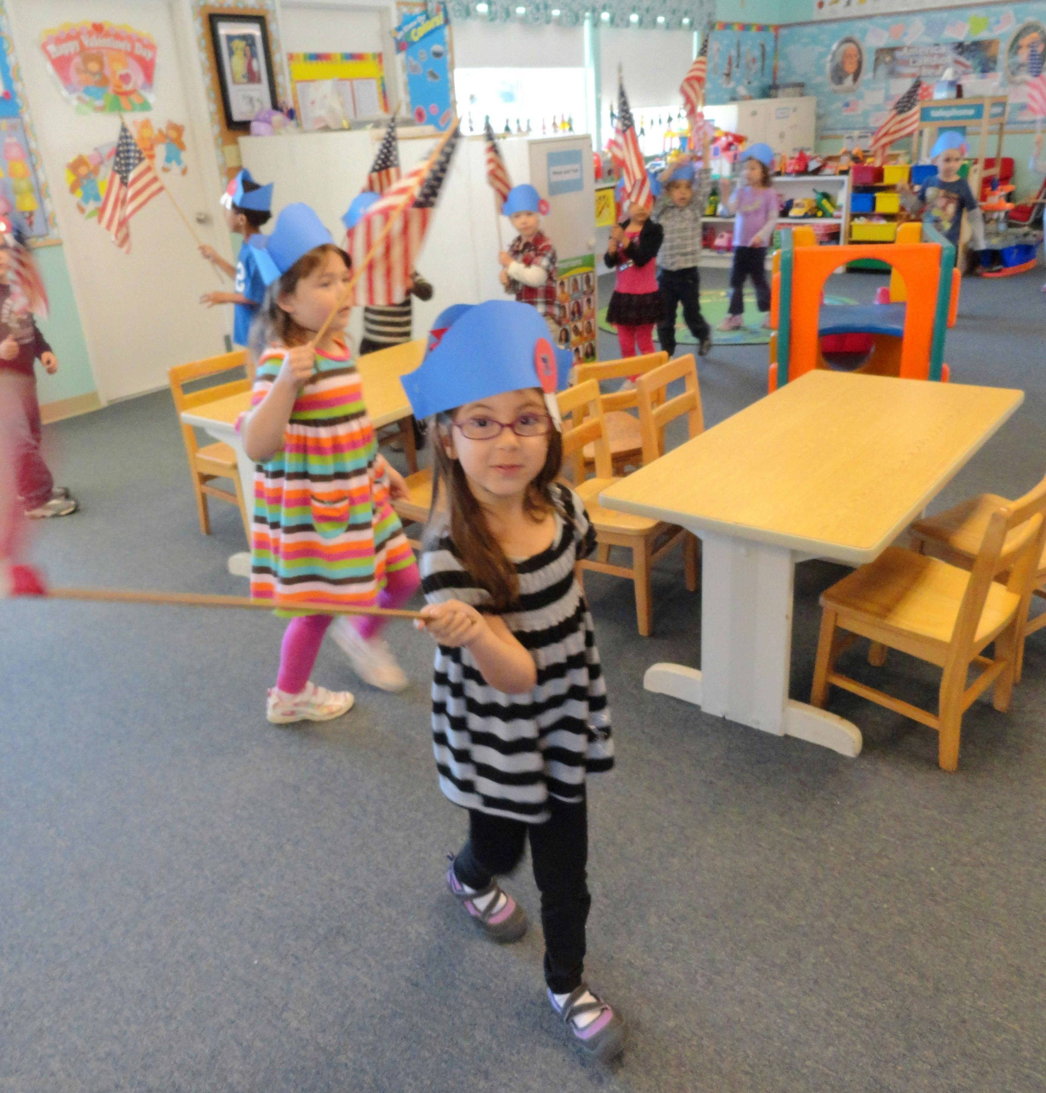 Children in a classroom wearing paper hats and holding flags