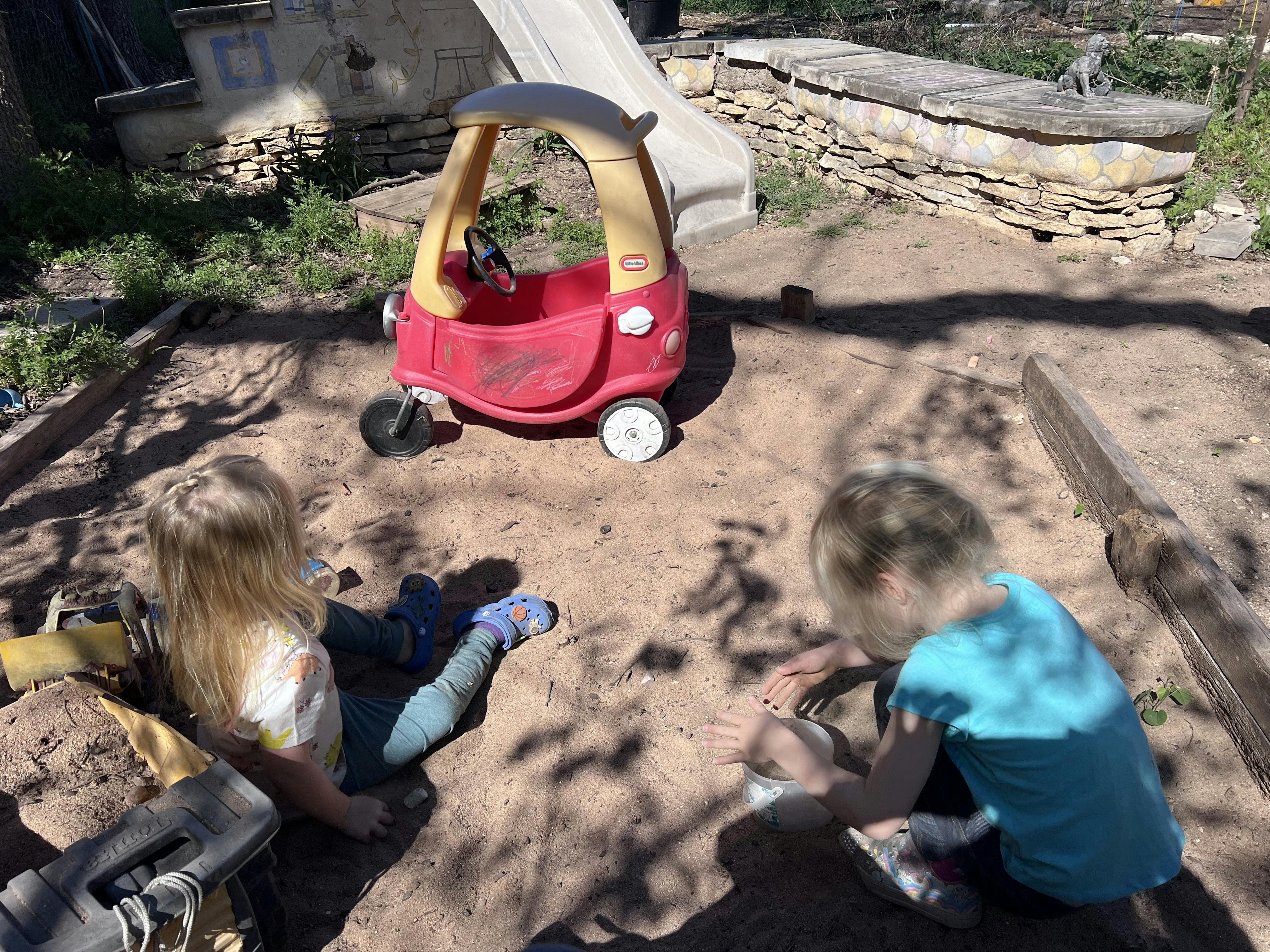 Two children playing in dirt next to a toy car