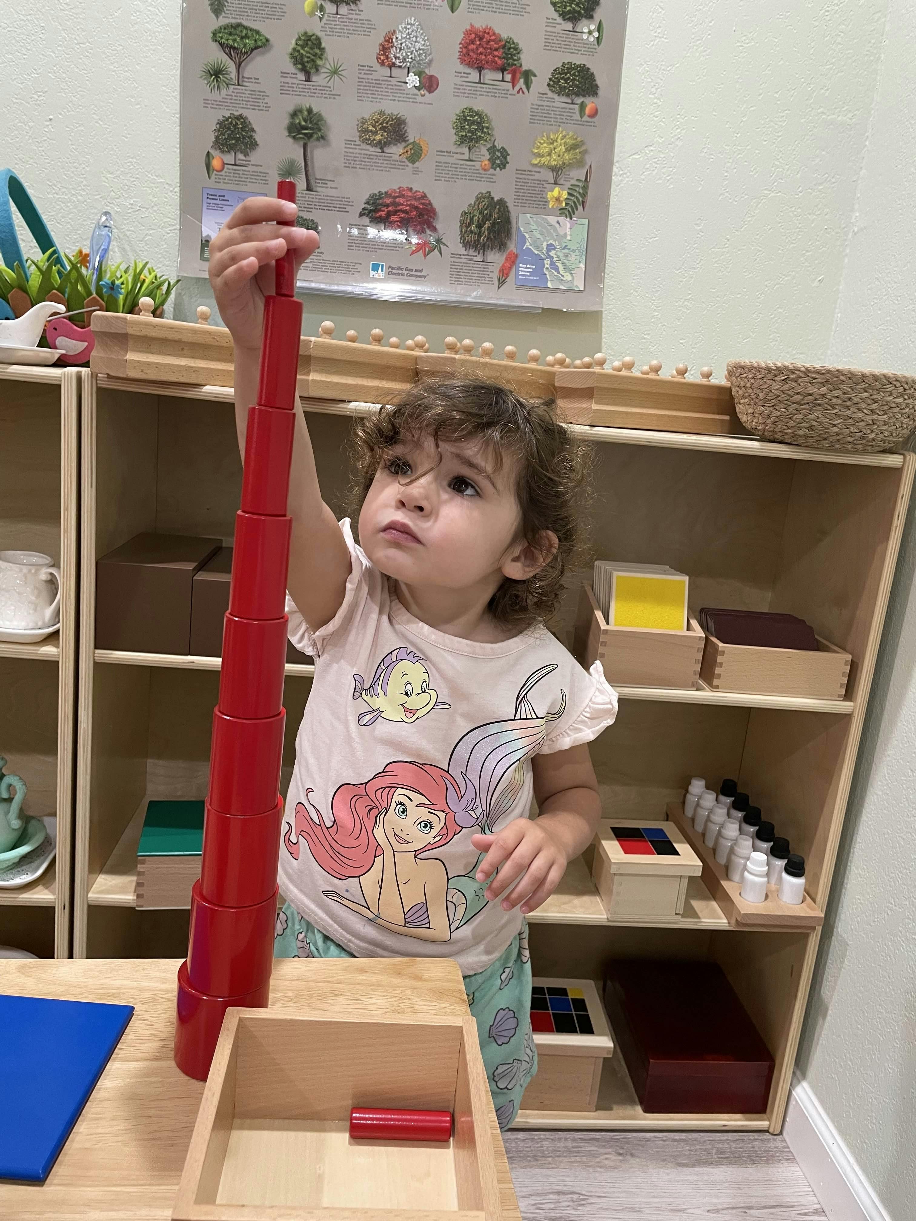 Child building a tall tower of red cylindrical blocks