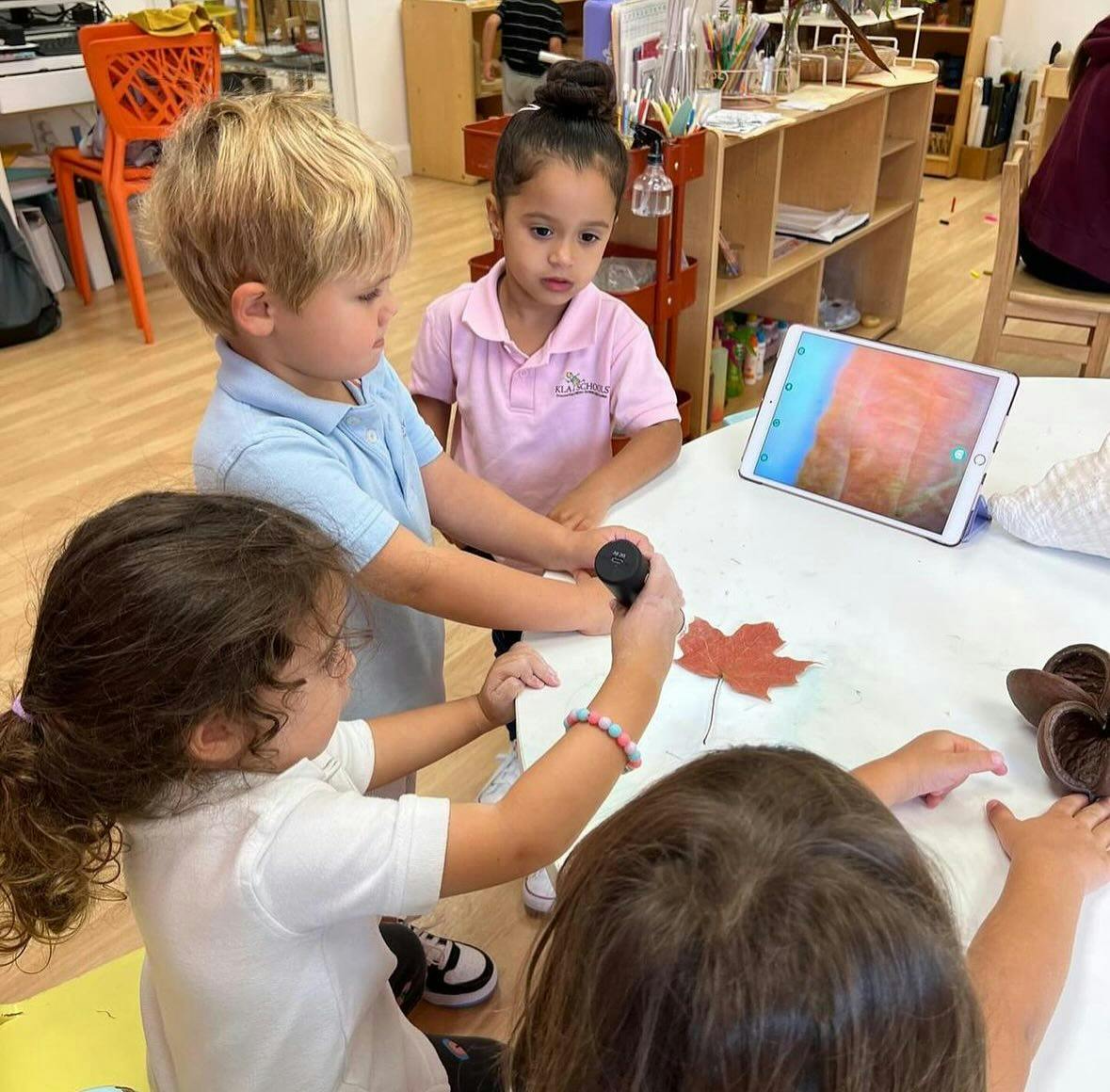 Children gathered around a table with a tablet and a leaf