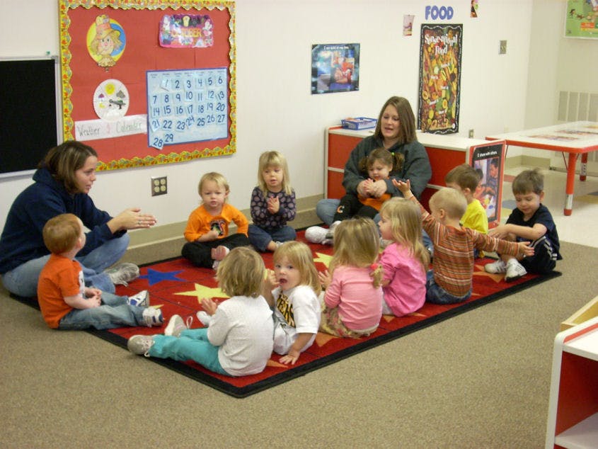 Two adults and multiple children sitting on a rug in a classroom