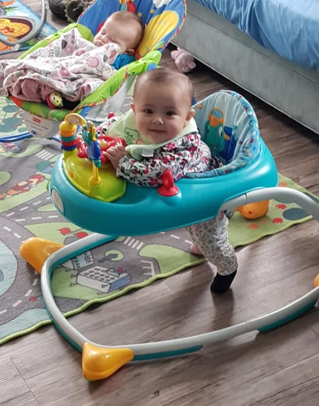 Baby in a walker with another baby in a bouncer in the background