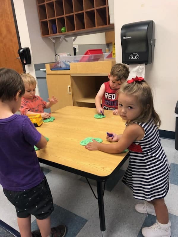 Children playing with green dough at a table in a classroom