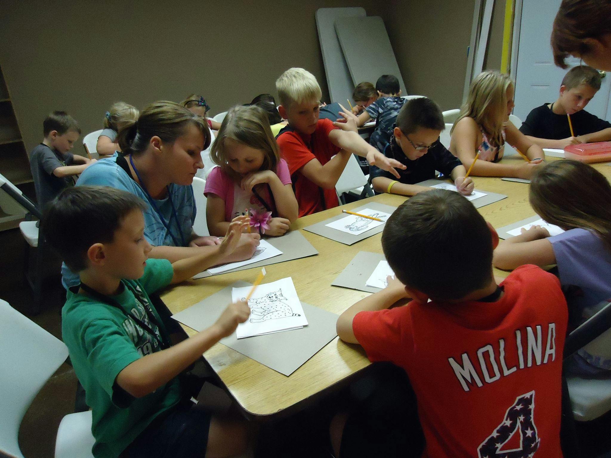 Adult and children writing at a table in a classroom