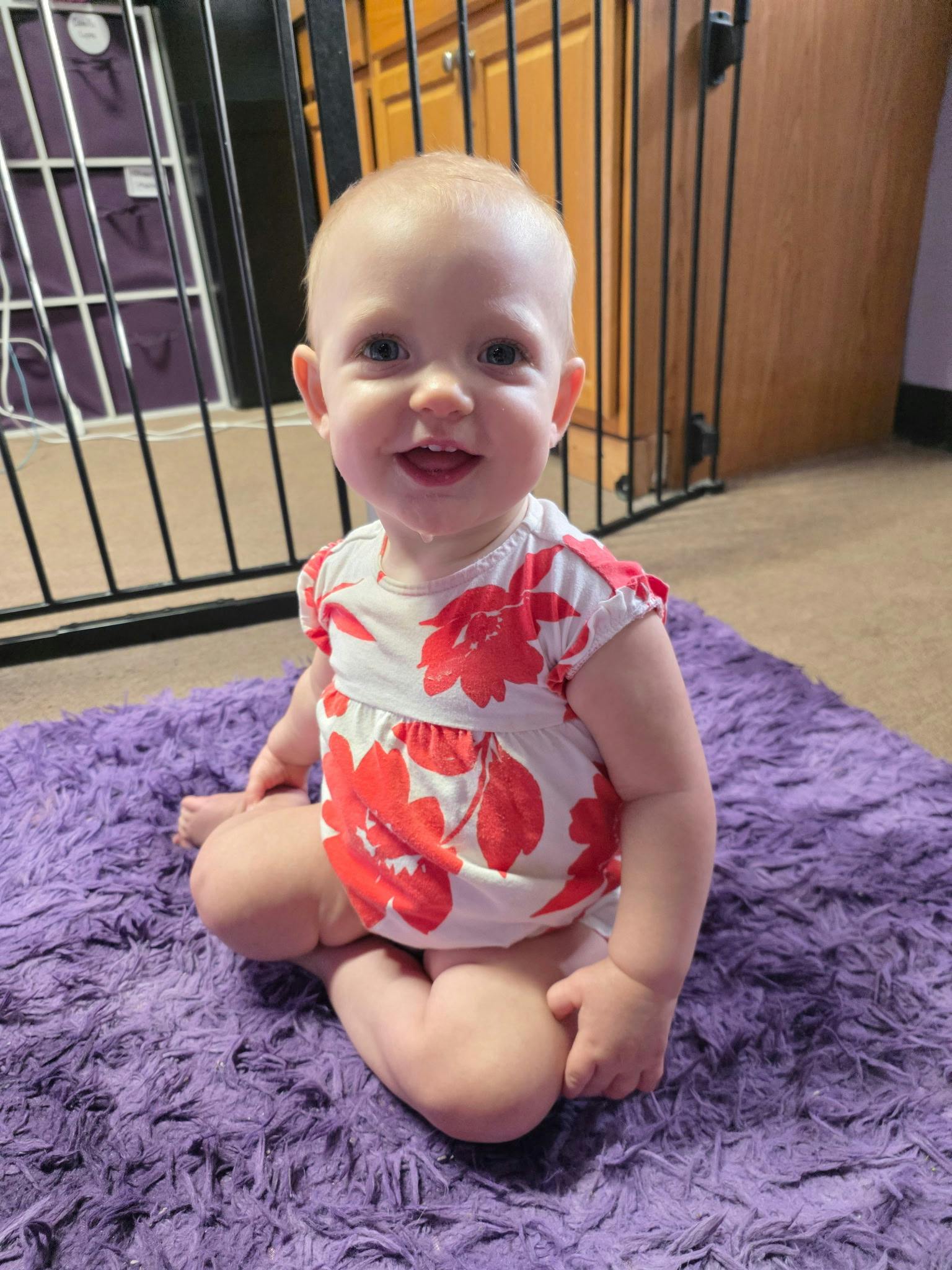 A baby sitting on a purple rug in front of a safety gate