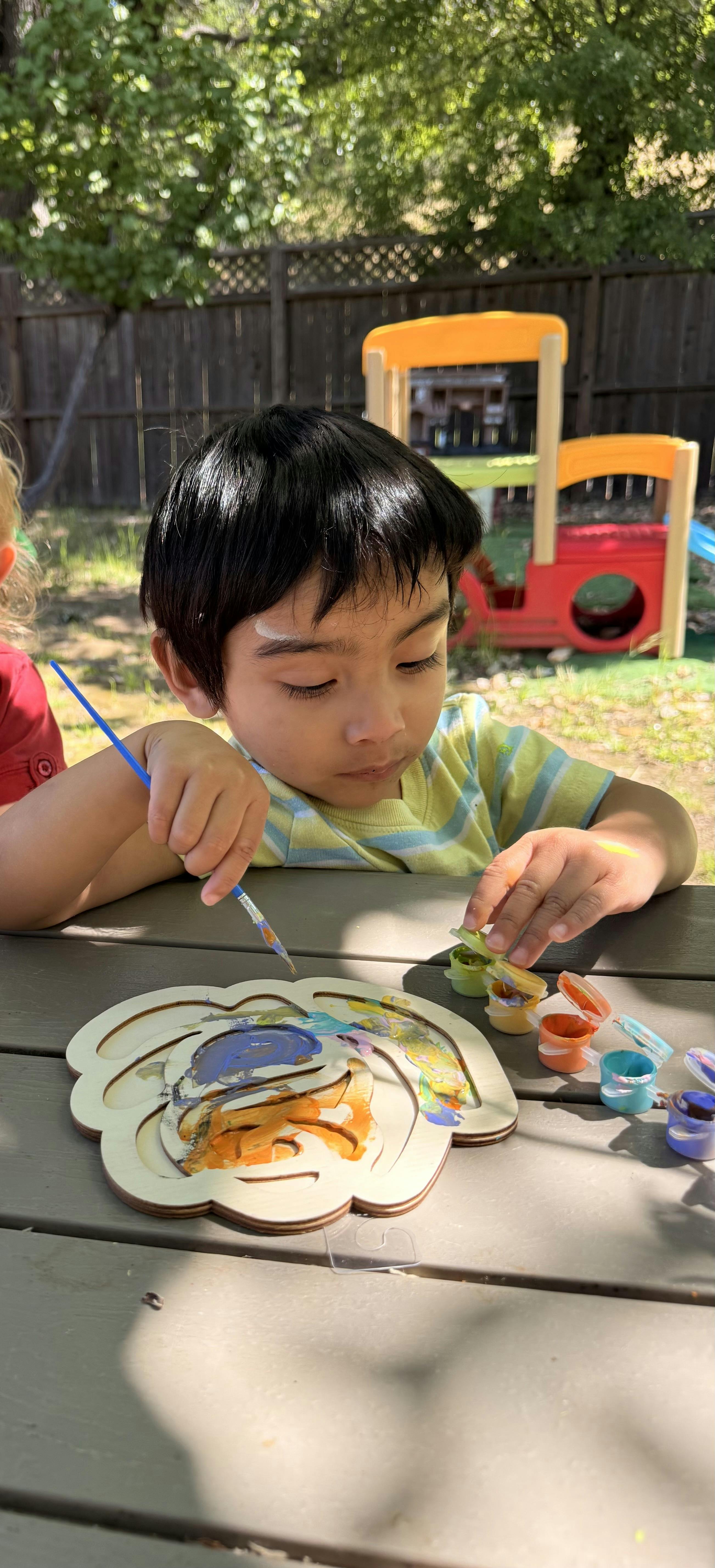Child painting a wooden cutout on a picnic table outdoors