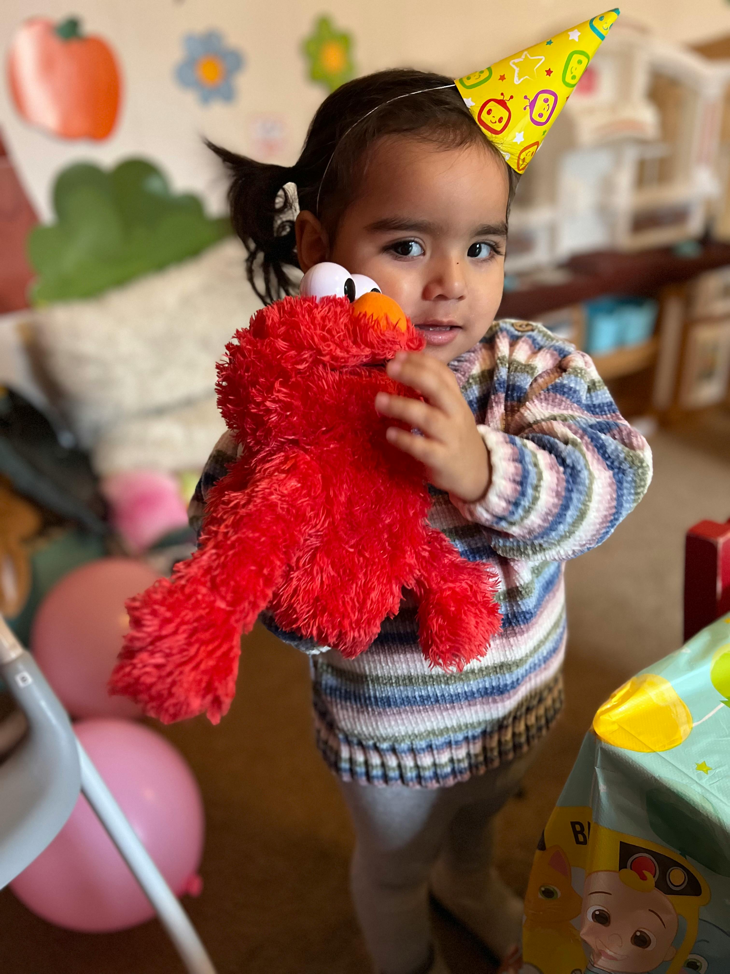 Child wearing a party hat and holding a red stuffed animal