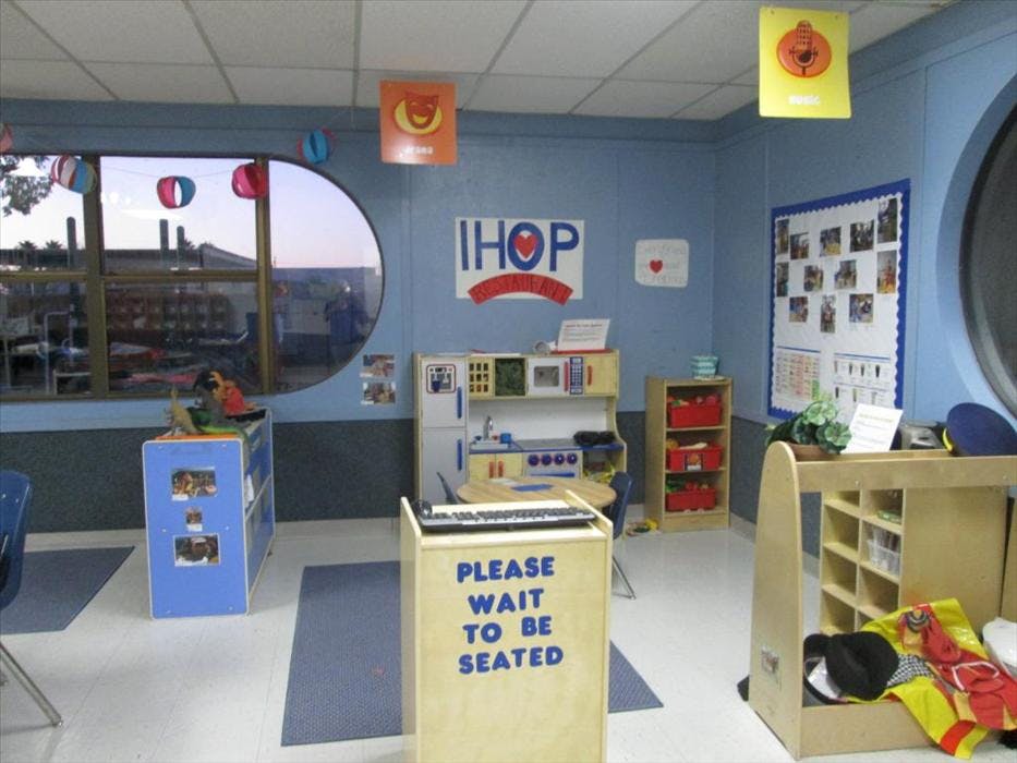 Classroom with play kitchen set and 'Please Wait to Be Seated' sign