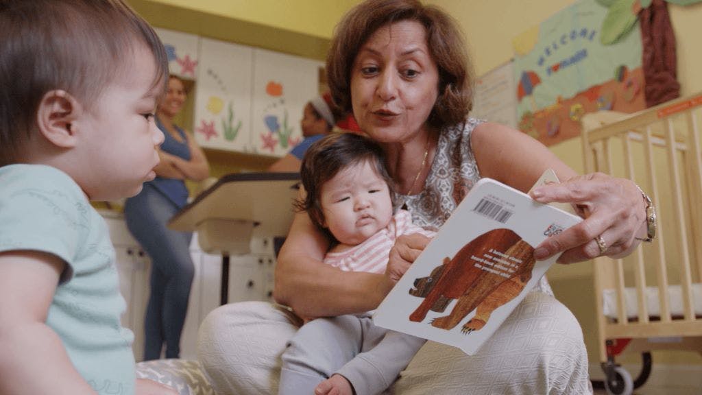 Person holding a child and reading a book to another child