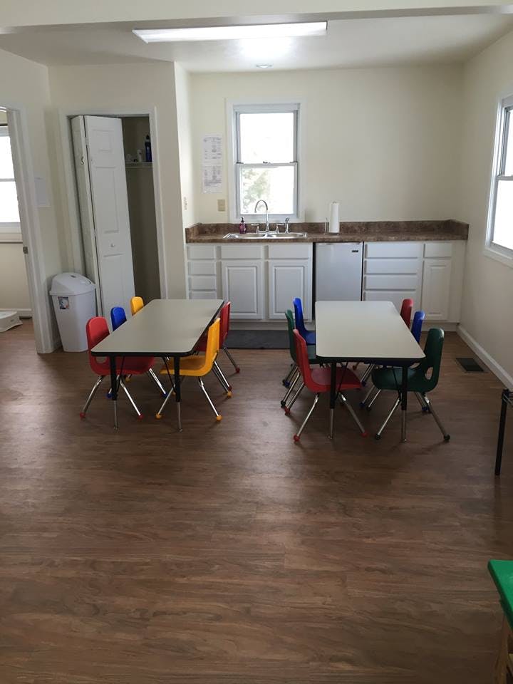 Classroom with small tables and colorful chairs, and a kitchen area